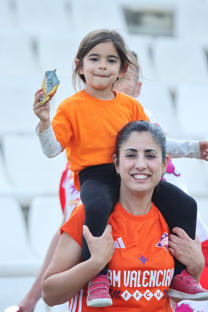 Madre con la camiseta AFICIÓ de la Selecció Valenciana y su hija a hombros animando en la grada