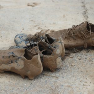 Botas de fútbol cubiertas de barro tras la dana de 2024 en un campo de l’Horta Sud