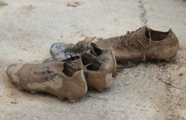 Botas de fútbol cubiertas de barro tras la dana de 2024 en un campo de l’Horta Sud