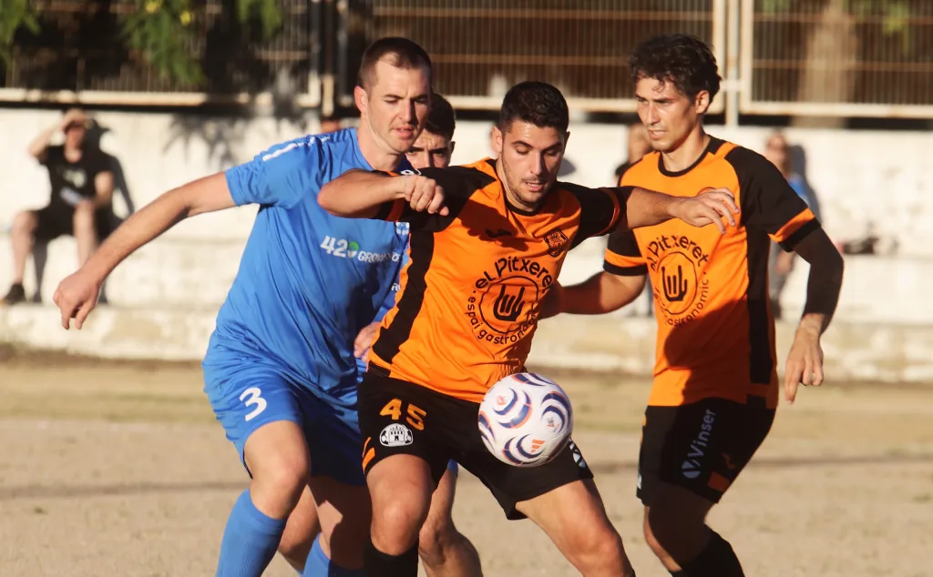 Jugadores del Quatretonda CF, de naranja, y del CD Albaidense, de azul, disputan el balón en Tercera FFCV